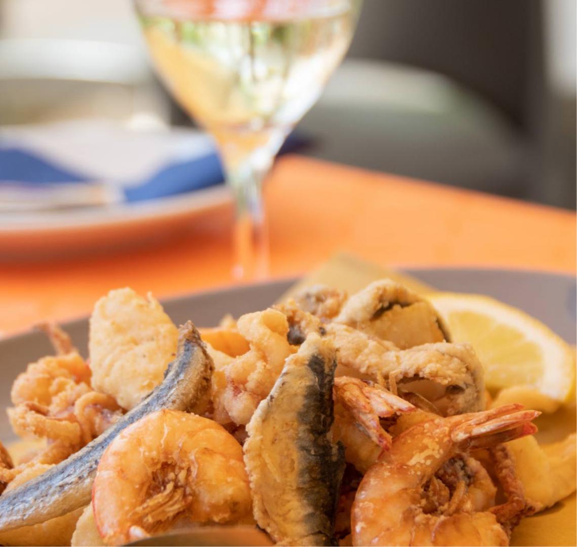 Frittura di pesce con gamberi e limone, accompagnata da un bicchiere di vino bianco.