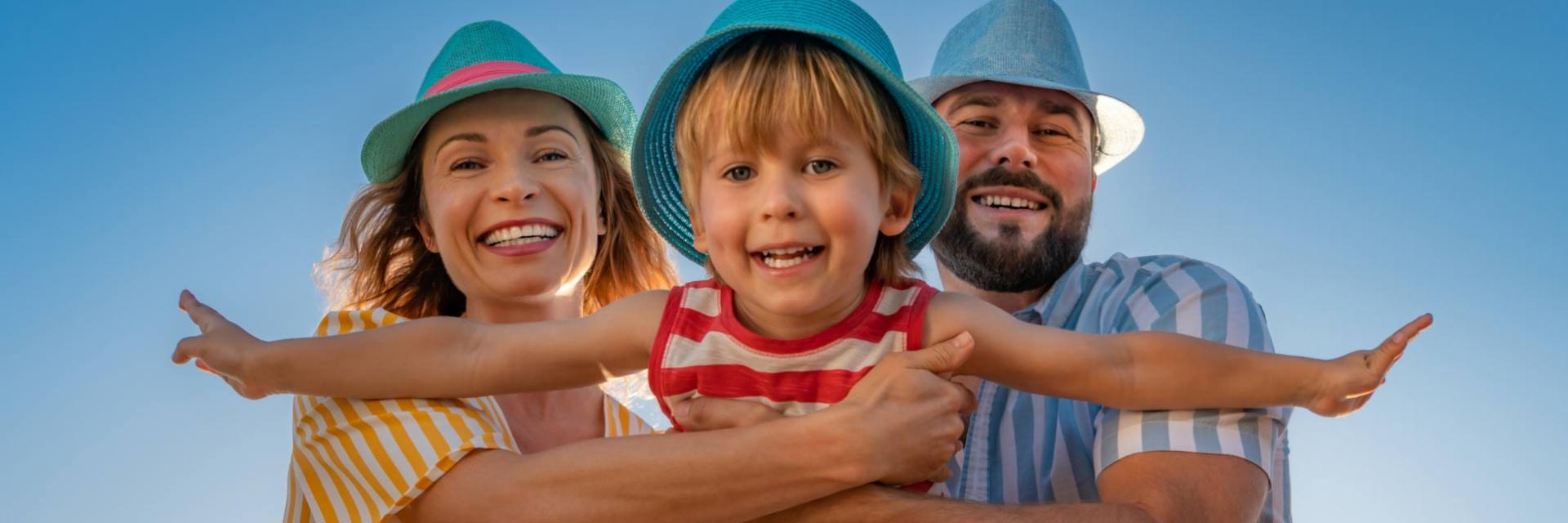 Famiglia felice con cappelli colorati, sorridono sotto il cielo blu.