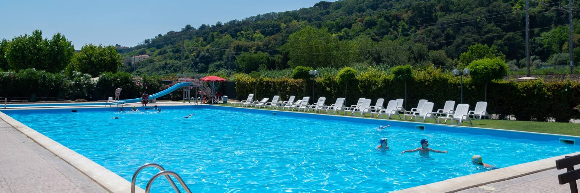 Piscina all'aperto con scivolo e lettini, circondata dal verde.