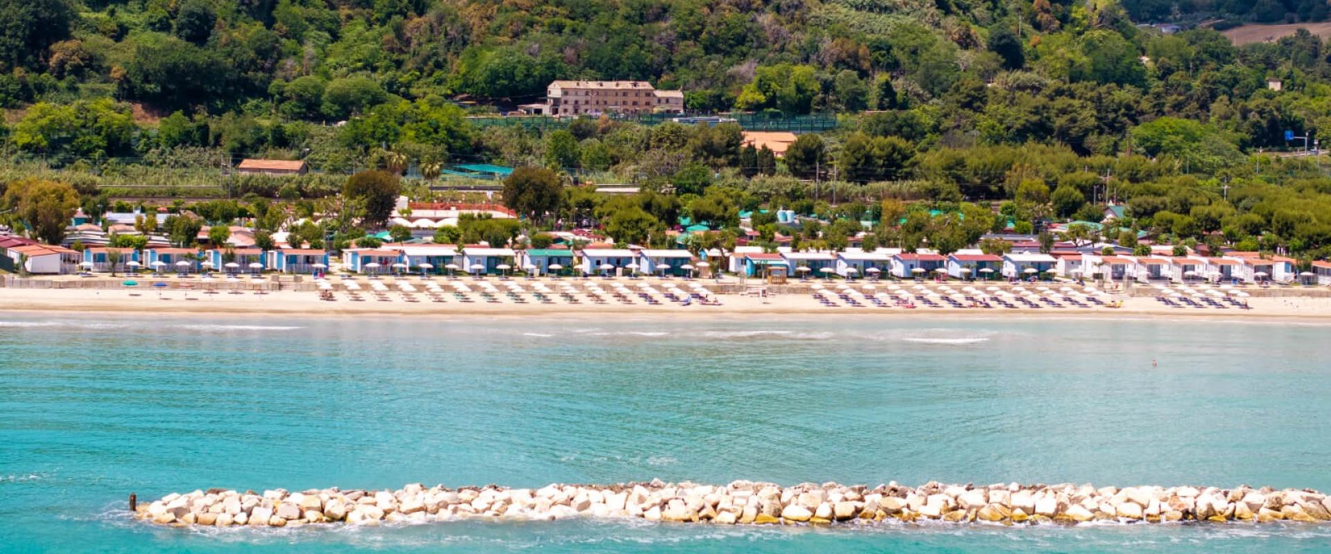 Spiaggia con ombrelloni e colline verdi sullo sfondo.