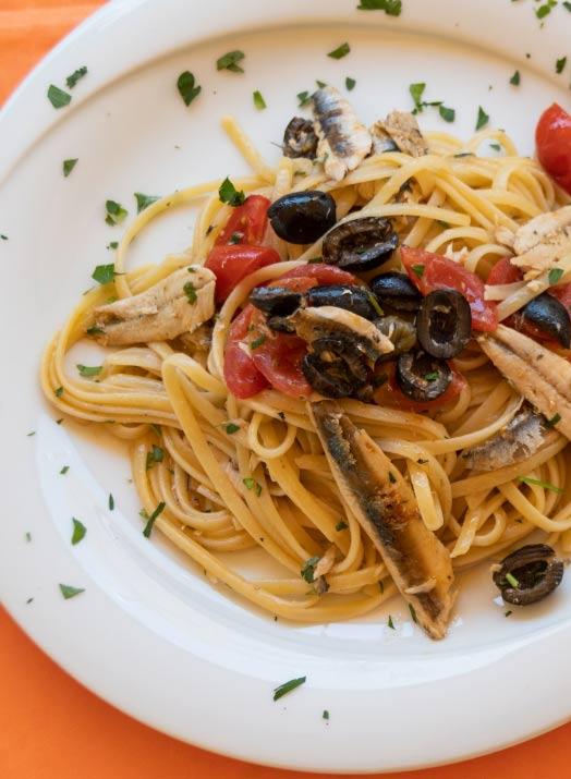 Pasta con acciughe, pomodorini, olive e prezzemolo, servita con vino bianco.