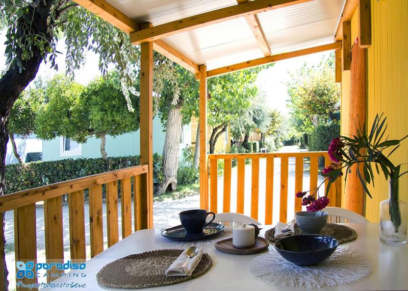Veranda accogliente con tavolo apparecchiato, circondata da alberi e natura.