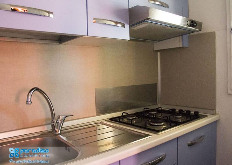 Cucina compatta con lavello, piano cottura a gas e cappa.