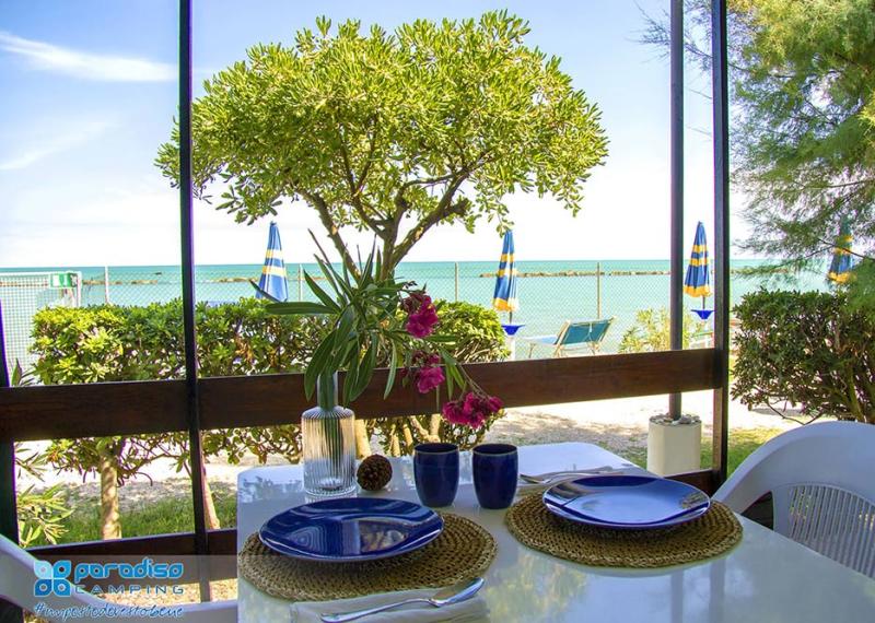 Vista mare da un campeggio con tavolo apparecchiato e ombrelloni sulla spiaggia.