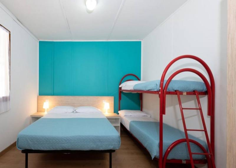 Camera semplice con letto matrimoniale e letti a castello, parete turchese.