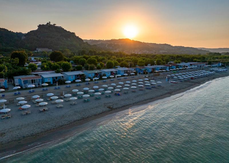 Spiaggia al tramonto con ombrelloni e villette sullo sfondo.